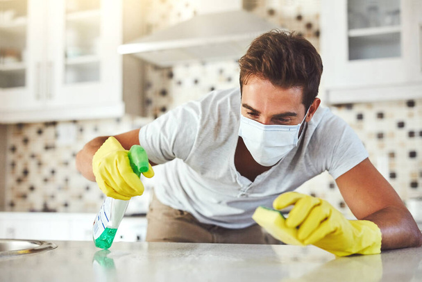 Δεν αφήνει ίχνη μικροβίων. Ένας όμορφος νεαρός καθαρίζει την κουζίνα του στο σπίτι. - Φωτογραφία, εικόνα