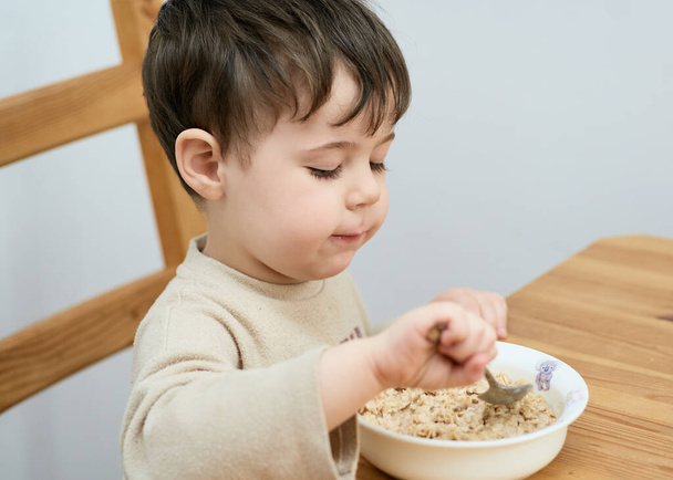 little boy eating oatmeal for breakfast in the kitchen - Photo, Image
