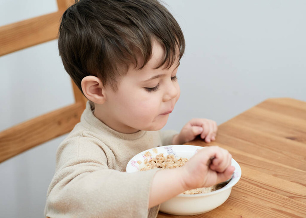 bambino che mangia farina d'avena per colazione in cucina - Foto, immagini