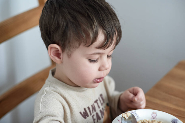 niño comiendo avena para desayunar en la cocina - Foto, imagen