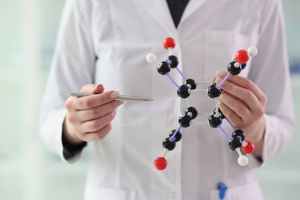 Химик в белом халате указывает ручкой на молекулярную модель, держащуюся за руки. Женщина-ученый представила структуру атомной системы на семинаре - Фото, изображение