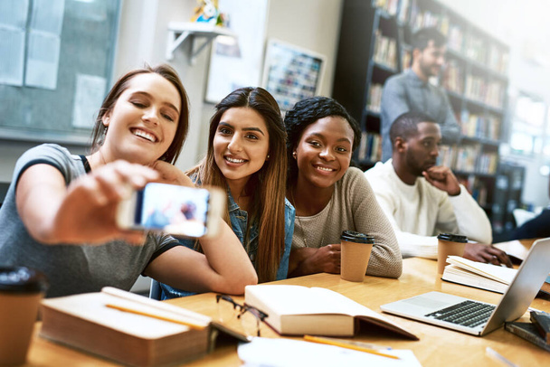 Vzdělání pro výhru. skupina mladých žen, které se společně věnují selfie při studiu v univerzitní knihovně - Fotografie, Obrázek