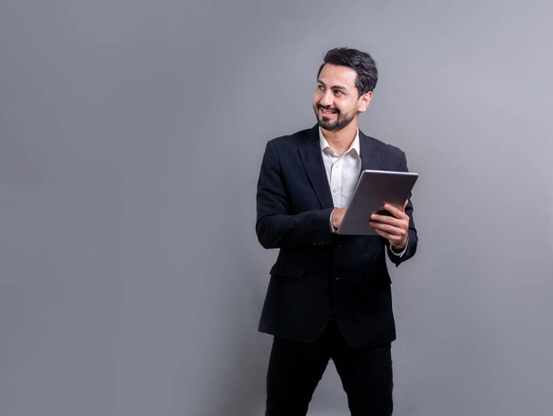 Confident businessman in formal suit holding tablet with surprise look for promotion or advertising. Facial expression and gestures indicate excitement and amazement on an isolated background. Fervent - Photo, Image