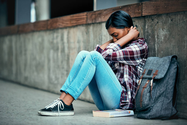 Νιώθω άγχος για τις εξετάσεις που πλησιάζουν. Μια νεαρή φοιτήτρια κάθεται στο πάτωμα και νιώθει κατάθλιψη έξω στο πανεπιστήμιο. - Φωτογραφία, εικόνα