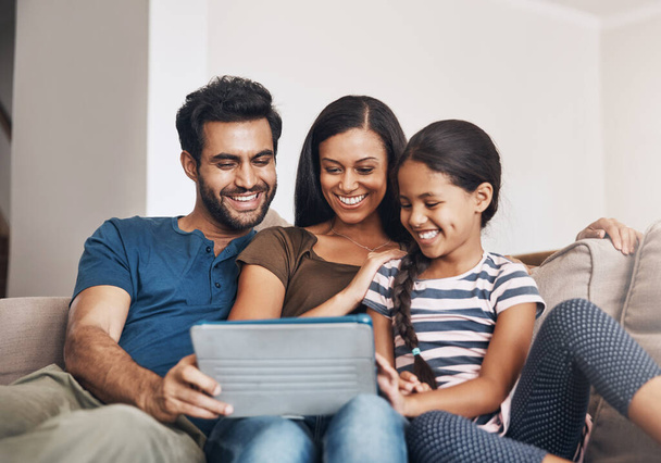 Hoe moderne gezinnen samenkomen. een moeder en vader met behulp van een digitale tablet met hun dochter op de bank thuis - Foto, afbeelding