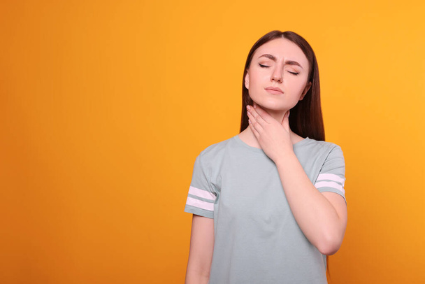 Young woman with sore throat on orange background. Space for text - Foto, afbeelding