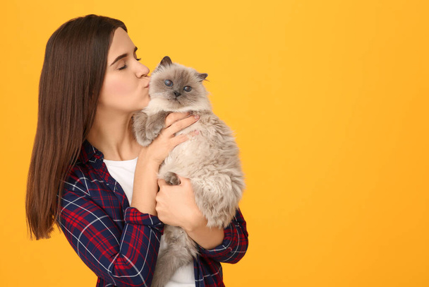 Woman kissing her cute cat on orange background, space for text - Фото, изображение