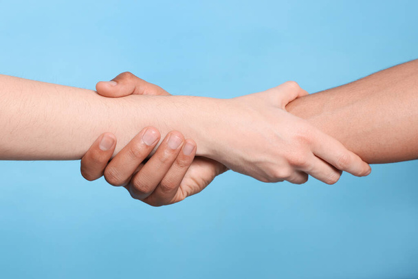 International relationships. People holding hands on light blue background, closeup - Fotoğraf, Görsel