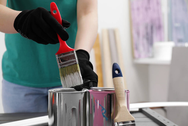Woman dipping brush into can of white paint at table indoors, closeup. Space for text - 写真・画像
