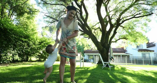 Mother holding baby child hands outside in idyllic backyard home garden during summer day - Foto, Imagen