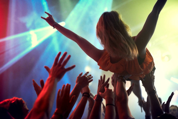 Concert, music festival and a woman crowd surfing at a club with lights and people in celebration. Group of men and women or fans at a rock or social event or show for live performance at a nightclub. - Photo, Image