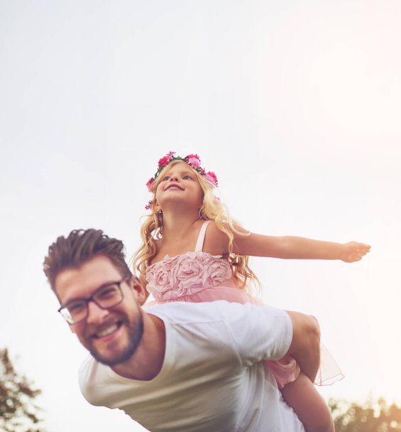 A minha pequena fada está a voar alto. um pai feliz dando a sua filha um passeio de piggyback fora na natureza - Foto, Imagem