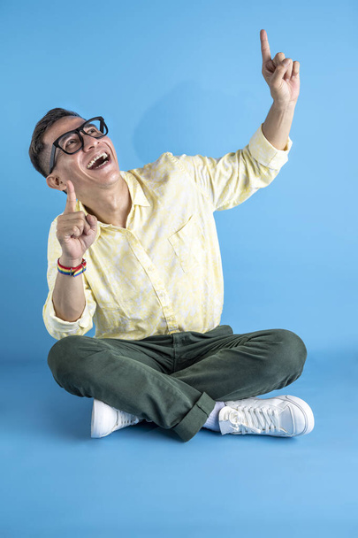 Homem com óculos e uma camisa usando uma pulseira de arco-íris apontando para algo em um fundo colorido - Foto, Imagem