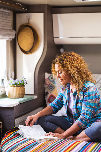 Relaxed young adult woman enjoying reading a book sitting comfortable on bed inside a camper van bedroom, People and indoor leisure activity alone. Travel and happiness. Little tiny house motor home - Foto, immagini