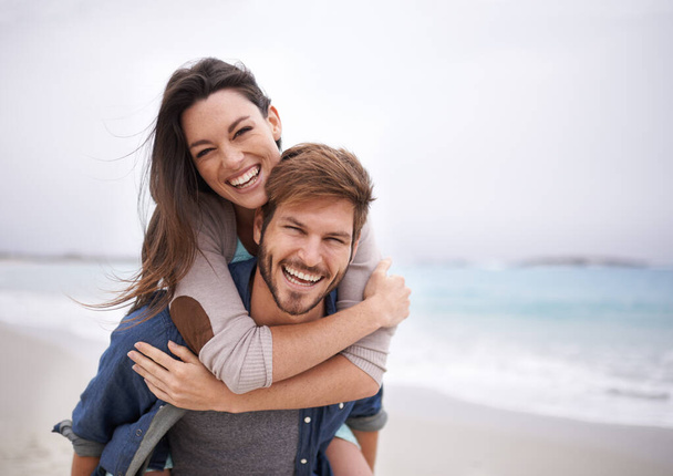 Love, piggyback and portrait of couple at a beach, hug and laughing while bonding outdoors. Face, embrace and happy man with woman at ocean for travel, freedom or vacation, holiday or Florida trip. - Fotografie, Obrázek