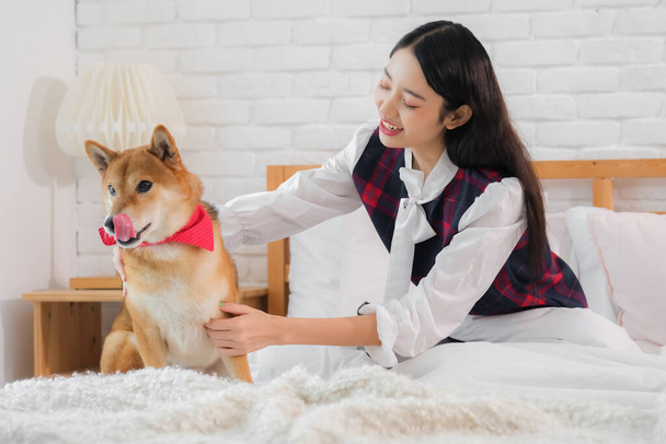 Любовь между красивой азиатской девушкой и ее собакой Shiba ощутимо, как они обнимаются друг с другом на кровати. - Фото, изображение