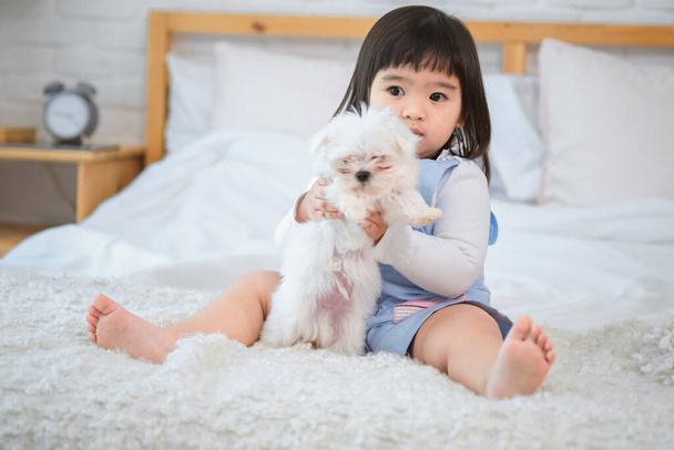Маленькая девочка держит белого пса близко к груди, чувствуя, что он мягкий мех против ее кожи. - Фото, изображение