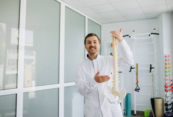 un vertebrologista sostiene un modelo de la columna vertebral en su mano - Foto, Imagen