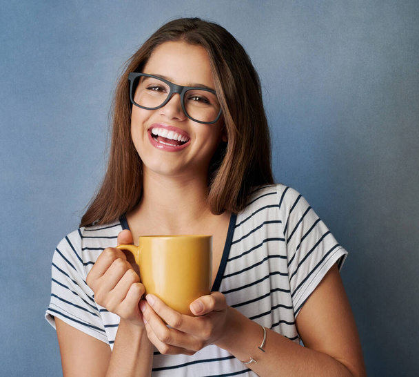 You just cant be grumpy with coffee in your hand. Studio shot of an attractive young woman holding a coffee mug against a gray background - Фото, изображение
