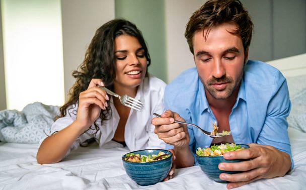 Happy young fit couple eating breakfast in bed in morning - Foto, Imagem