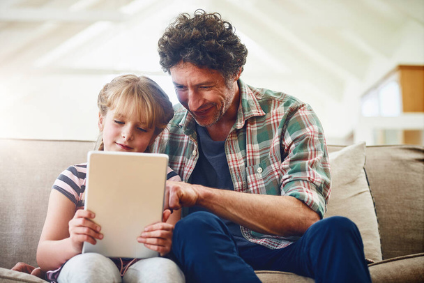 Buscando novos e emocionantes aplicativos para baixar. um pai e sua filhinha usando um tablet digital em casa - Foto, Imagem
