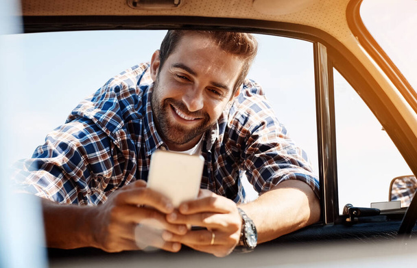 Maybe I can meet up with friends who are nearby. a handsome man sending a text while enjoying a road trip - Fotoğraf, Görsel