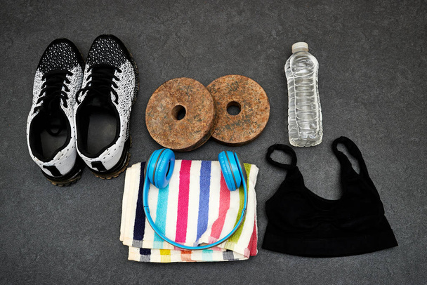 Healthy lifestyle, sport or athlete's equipment set : man or woman clothing and bottle of water with blue wireless headphone and dumbbell, sneakers and towel on gray background - Photo, image