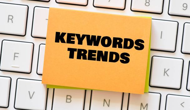 KEYWORDS TRENDS words on a small piece of paper placed on a white keyboard. - Photo, Image