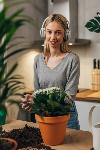 Portrait of a young blond woman with headphones potting a plant. - Foto, Bild