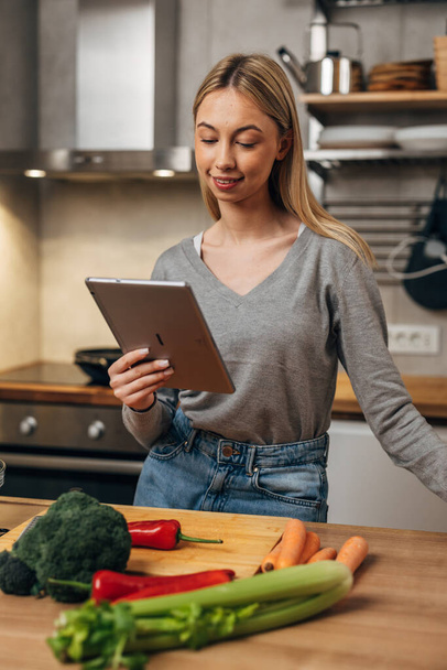 A young woman is reading a recipe using digital tablet. - Foto, imagen