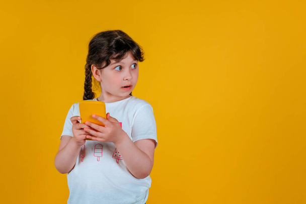 Copyspace foto de uma menina encaracolado bonito alegre encantador segurando um telefone em suas mãos isolado em um fundo de cor brilhante - Foto, Imagem