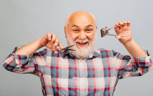 Old hairdresser. Happy old bearded man, bearded male with scissors and straight razor hair clipper - 写真・画像