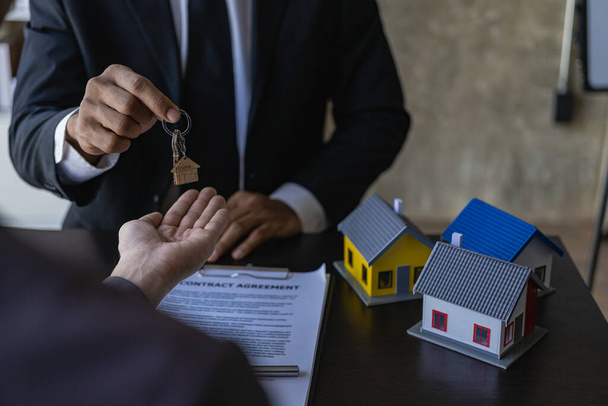Real estate agents offer contracts to buy or rent housing. Businessman holding model small building house with property insurance at table in home sales office - Fotó, kép