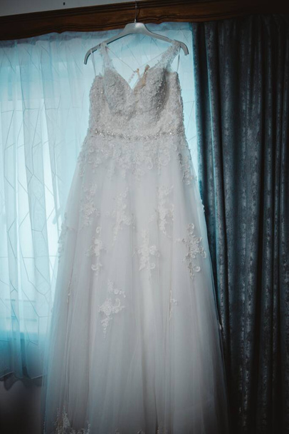 A bridal gown hanged alongside window curtains - Zdjęcie, obraz