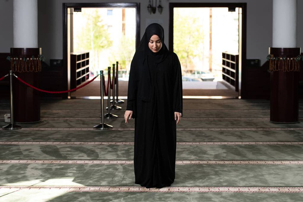 A beautiful Muslim woman in a black dress with hijab praying in a mosque. - Foto, immagini