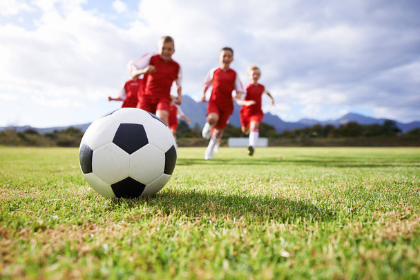Τρέξιμο, ομαδική εργασία και αθλήματα με παιδιά και μπάλα ποδοσφαίρου στο γήπεδο για την κατάρτιση, τον ανταγωνισμό και την καλή φυσική κατάσταση. Παιχνίδι, καλοκαίρι και δράση με ποδοσφαιριστή και κλωτσιά στο γήπεδο για τους στόχους, την ενέργεια και τον αθλητή. - Φωτογραφία, εικόνα