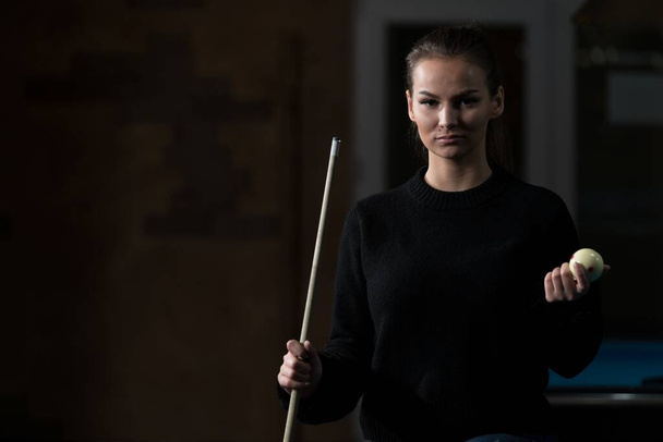 A young Caucasian woman holding a pool cue and a ball during a pool game - Fotografie, Obrázek