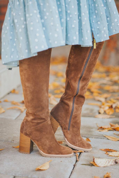 A cozy lady wearing brown leather boots while walking on a street with autumnal leaves - Foto, Bild