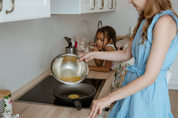 台所の電気ストーブの上で母親とパンケーキを作る女の子 - 写真・画像