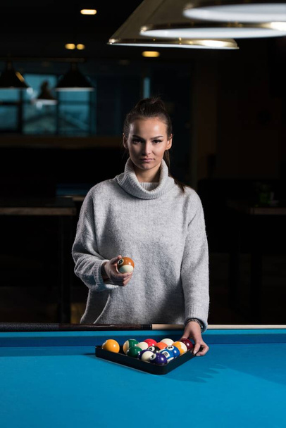 A young woman standing at the pool table arranging billiard balls in a triangle. - Foto, Bild