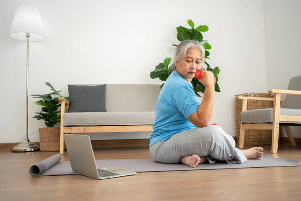 Asian senior woman lifting dumbbell for exercise and workout at home. Active mature woman doing stretching exercise in living room. Exercise Active and healthy for older, elder, and senior concept. - Fotografie, Obrázek