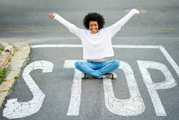 Some say the fearless are truly free. a happy young woman sitting on a stop sign at an intersection - Foto, imagen