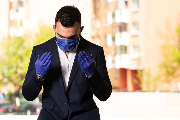 A young Muslim man praying outdoors while wearing a protective mask and gloves - Foto, Imagen