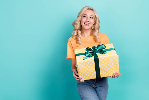 Photo of funny dreamy girl wear orange t-shirt holding gift looking empty space isolated turquoise color background. - Φωτογραφία, εικόνα