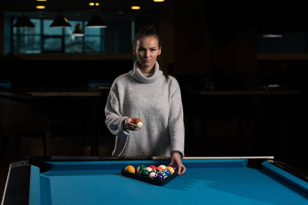 A young woman standing at the pool table arranging billiard balls in a triangle. - Fotografie, Obrázek
