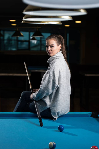 A vertical shot of a young woman sitting on the pool table. - Foto, imagen