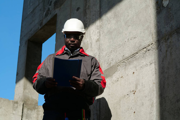 Африканский рабочий стоит на стройке с рабочими документами - Фото, изображение
