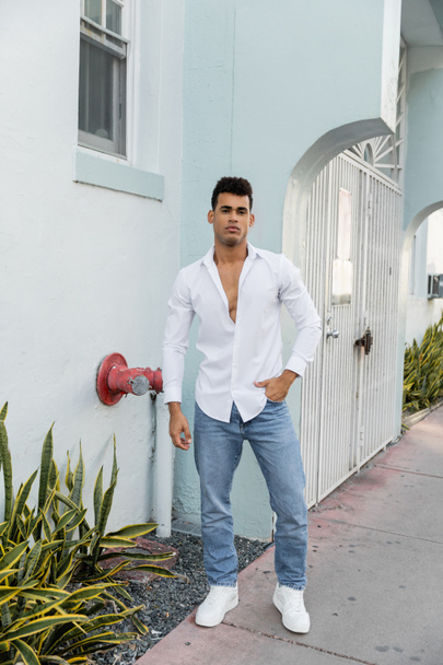 Longitud completa del joven hombre cubano en camisa elegante y jeans azules posando en la calle en Miami - Foto, Imagen