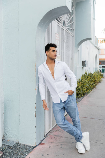 In voller Länge posiert ein hübscher kubanischer Mann in stylischem Hemd und blauer Jeans auf der Straße in Miami - Foto, Bild