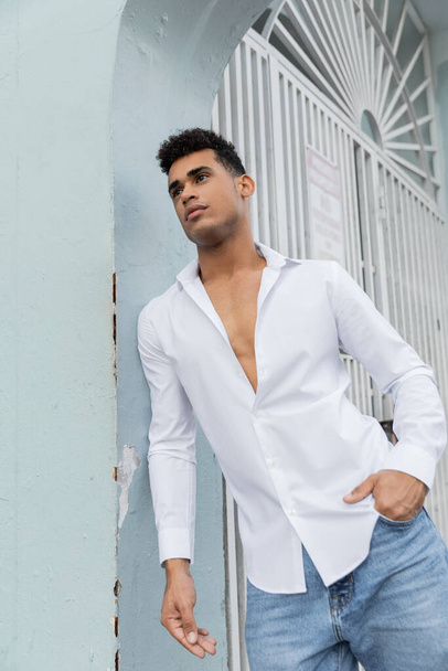 przystojny i kręcone kubański człowiek w stylowy koszula i niebieski dżinsy pozowanie na ulicy w Miami - Zdjęcie, obraz